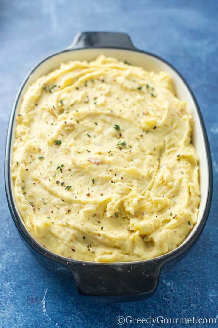 Mash potato in a serving dish sprinkled with herbs and salt and pepper.