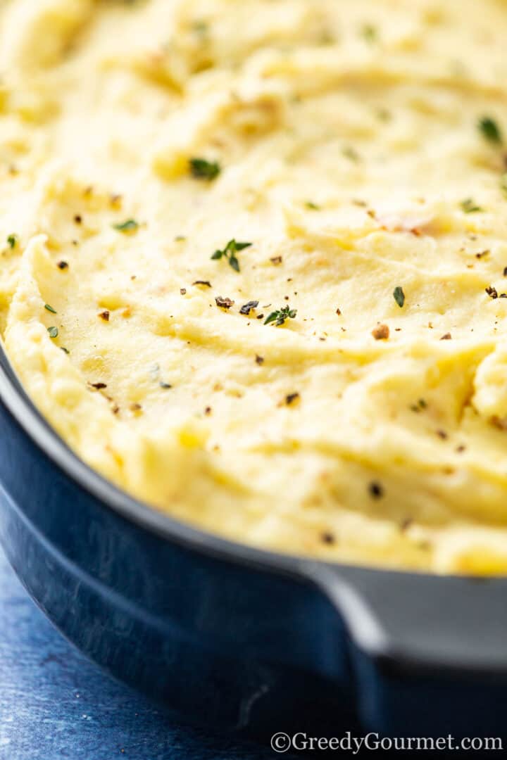 Mash potato in a serving dish sprinkled with herbs and salt and pepper.