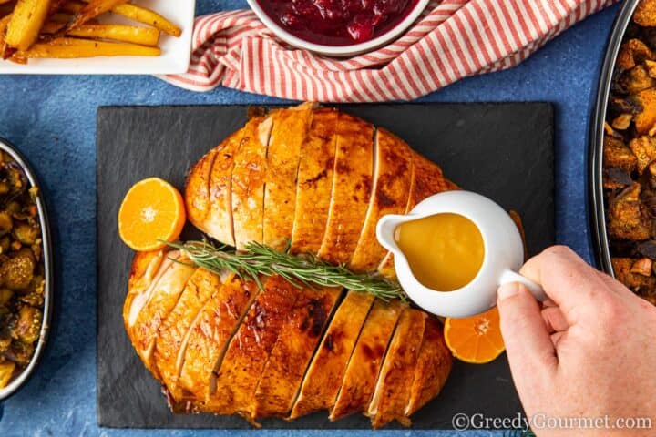 pouring simple turkey gravy over a cooked turkey.