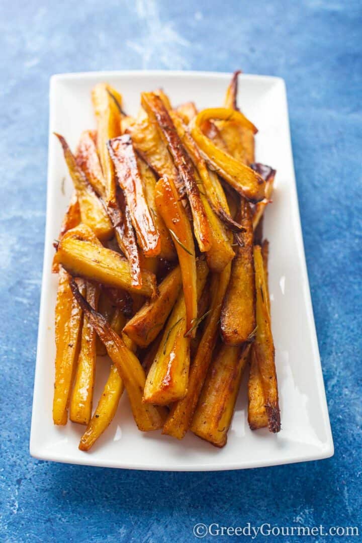golden honey roasted parsnips on a white serving dish.