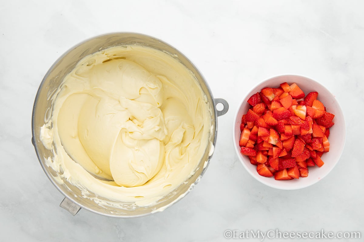 bowl of cheesecake filling next to a bowl of cut up strawberries.