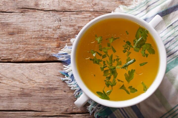 beef broth in a white bowl on wooden background.