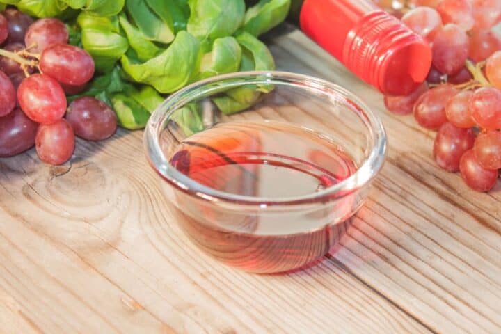 Red wine vinegar in glass  bowl surrounded with grapes