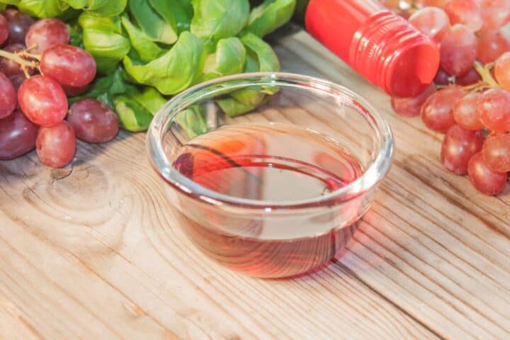 Red wine vinegar in glass bowl surrounded with grapes