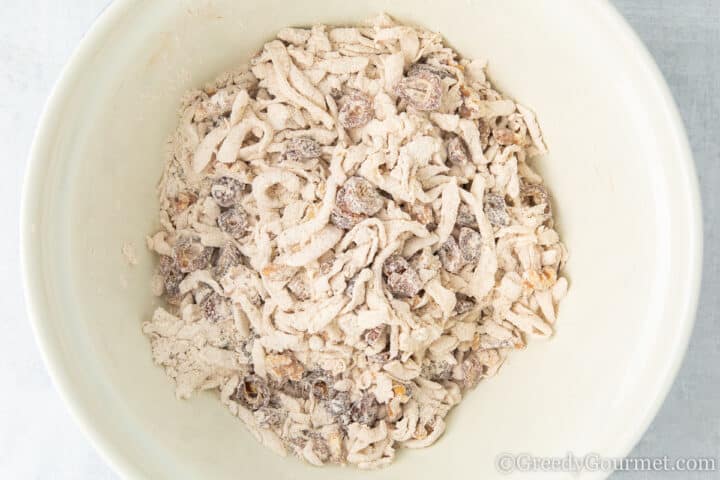 Mixing marrow, flour, dates and walnut in a white bowl.