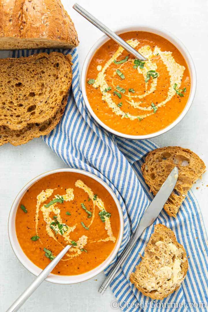 marrow and tomato soup in a white bowl with a slice of buttered bread next to it. 