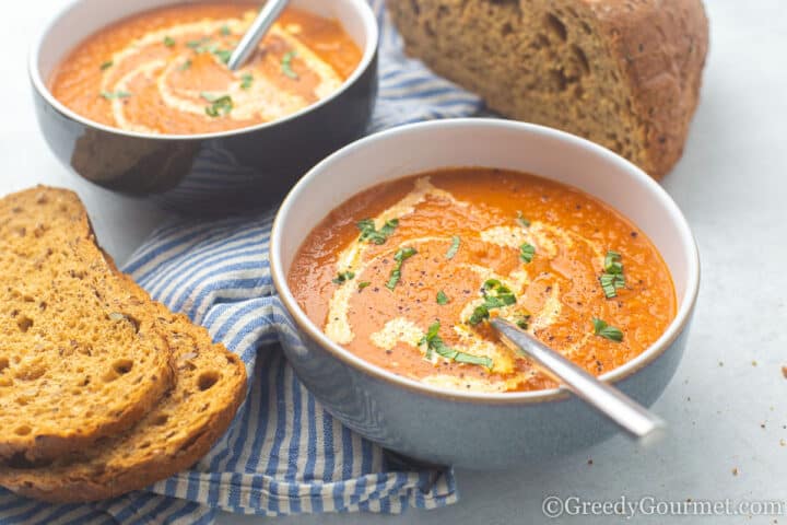 marrow and tomato soup in a bowl with bread beside the bowl
