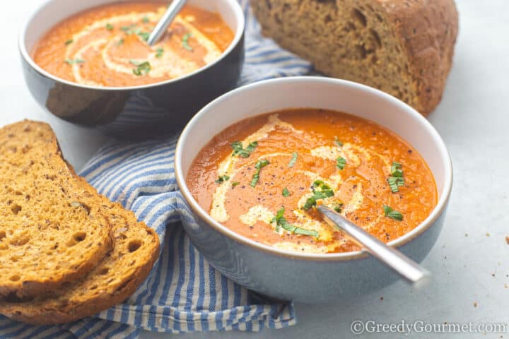 marrow and tomato soup in a bowl with bread beside the bowl