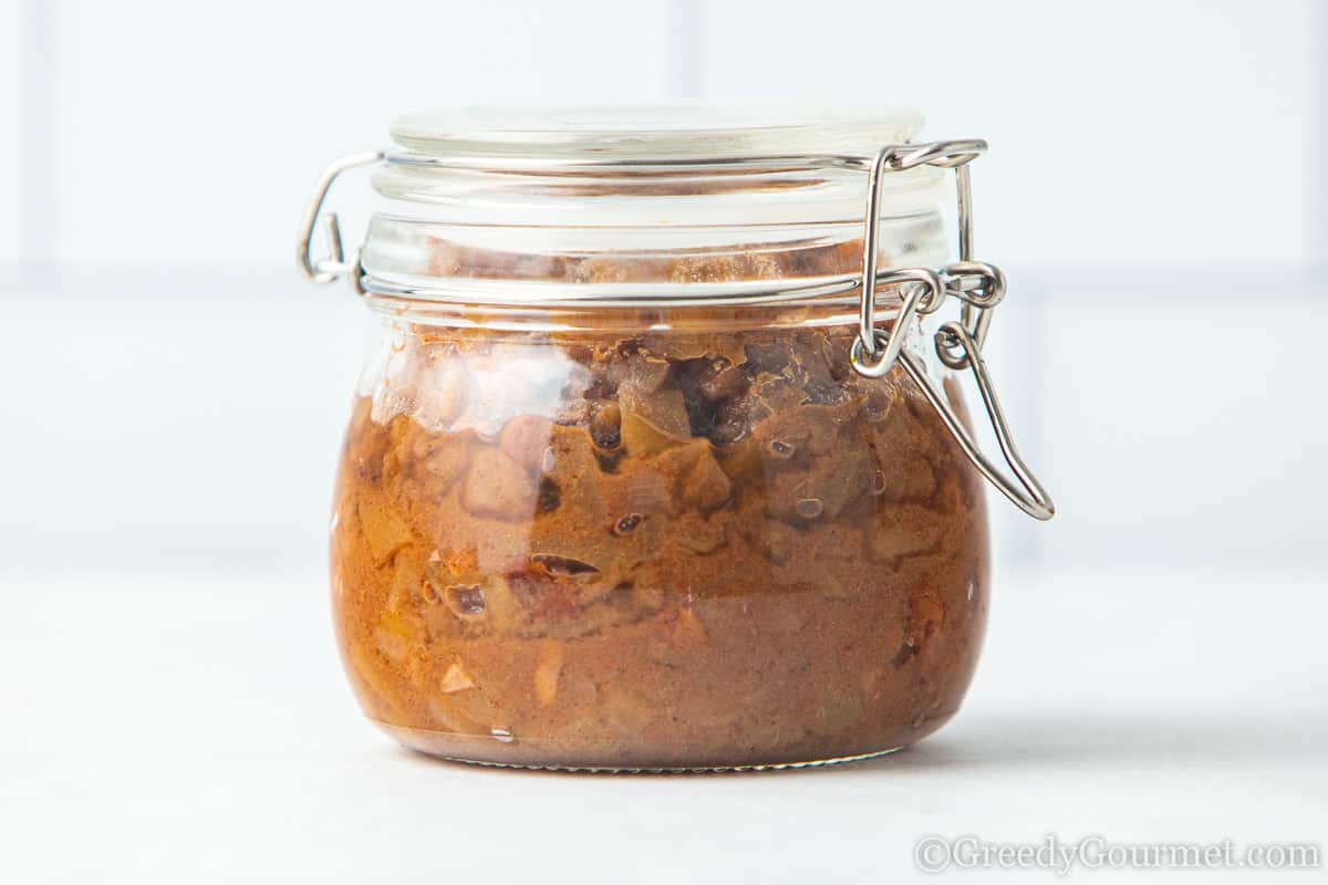 glass jar of pear chutney by itself on a white table.