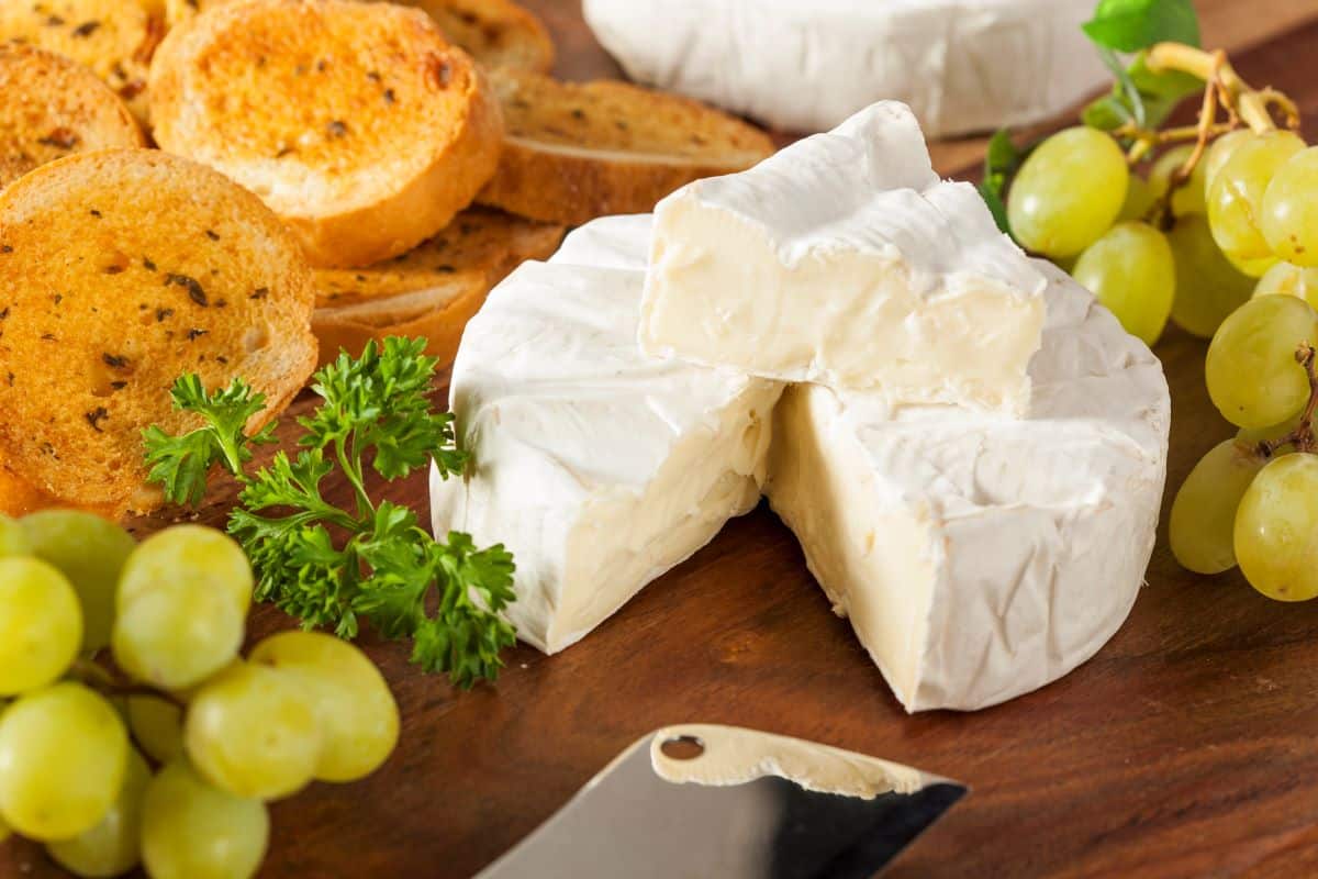 Brie slices on a board with grapes and bread.