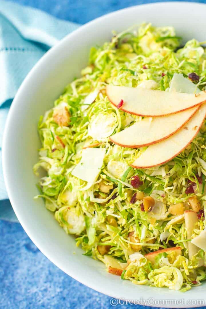 brussels sprouts salad in a bowl topped with apple slices.