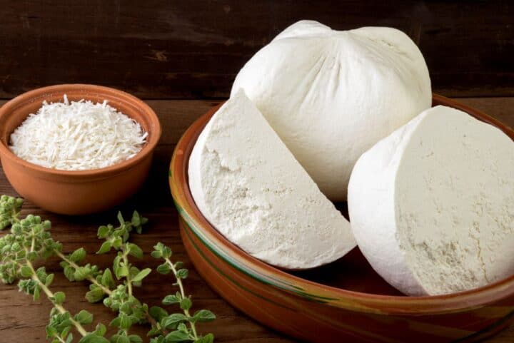 bowl with mizithra cheese and herbs laid beside it