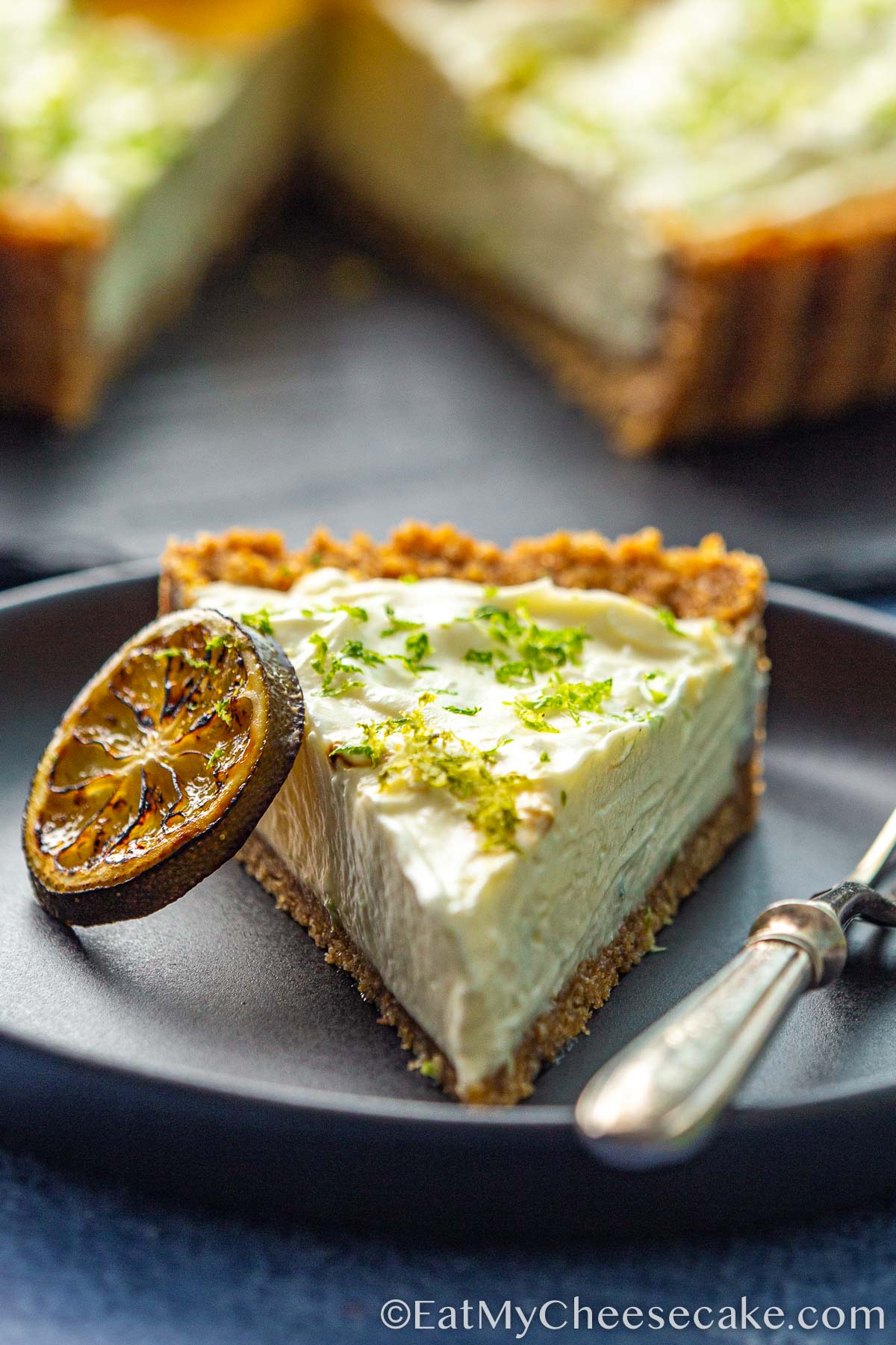 Slice of key lime cheesecake pie decorated with lime slices and lime zest.