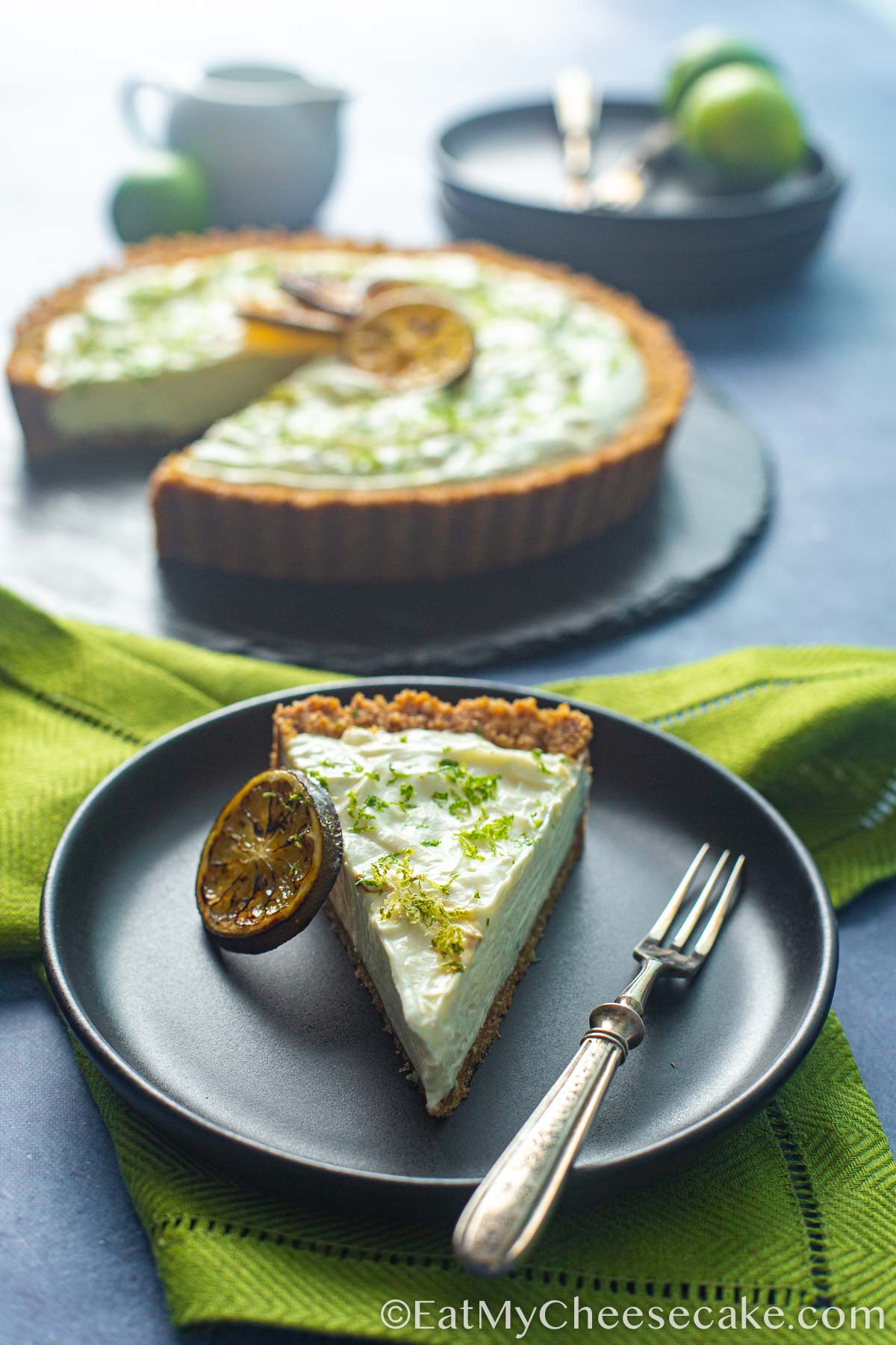 Slice of key lime cheesecake pie decorated with lime slices and lime zest.