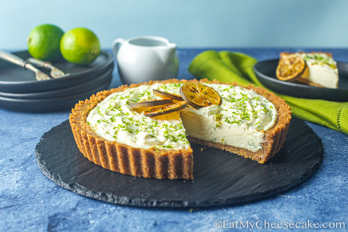 Key lime cheesecake pie decorated with lime slices and lime zest with a slice taken out..