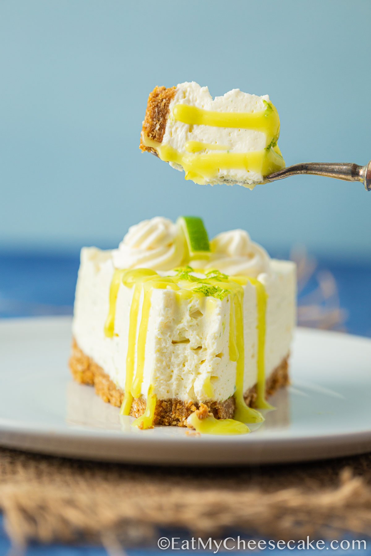 Slice of no bake lime cheesecake with lime curd drizzled on top. and a bite taken out