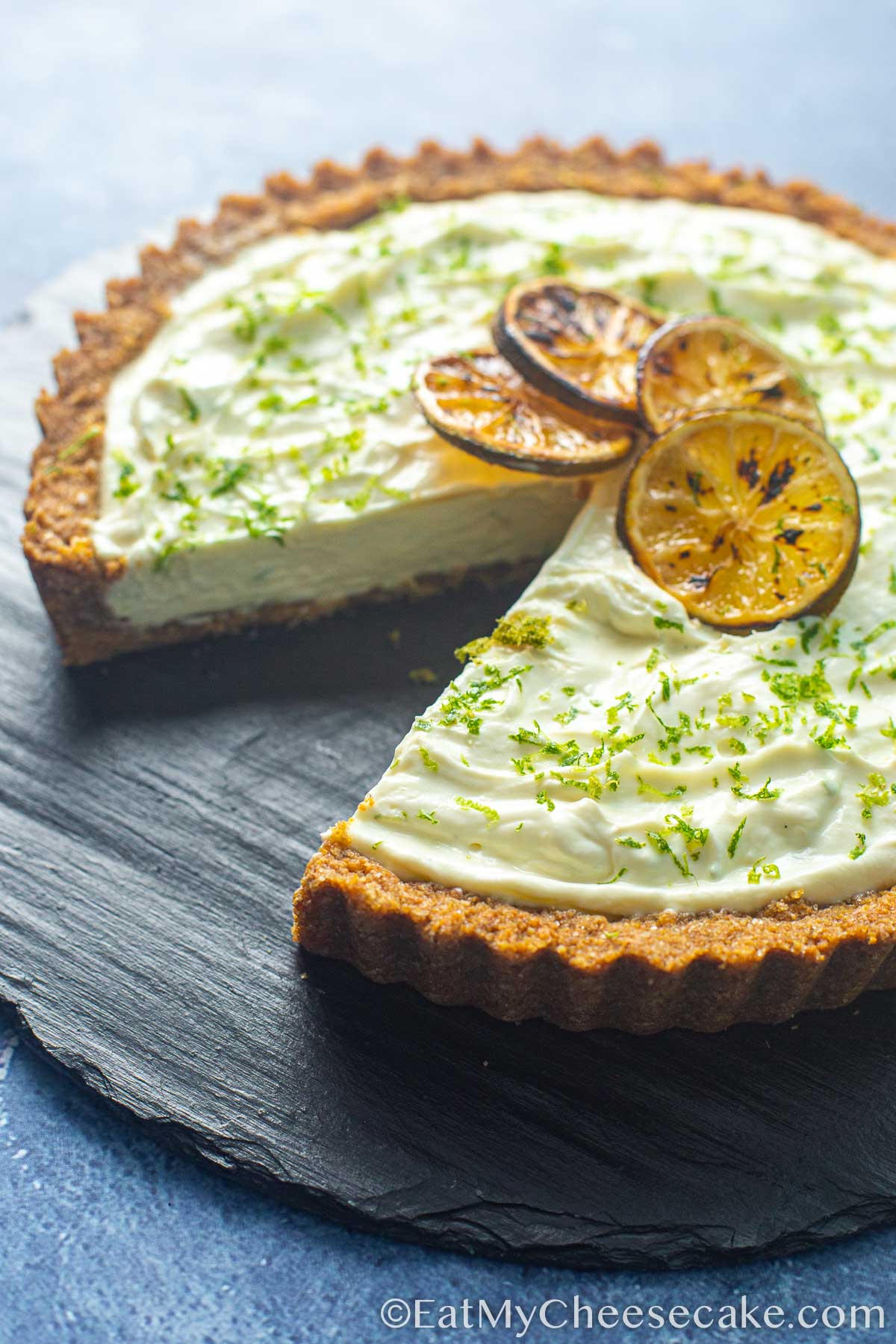 Key lime cheesecake pie decorated with lime slices and lime zest and a slice taken out.