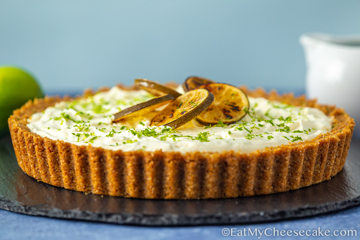 Slice of key lime cheesecake pie decorated with lime slices and lime zest.