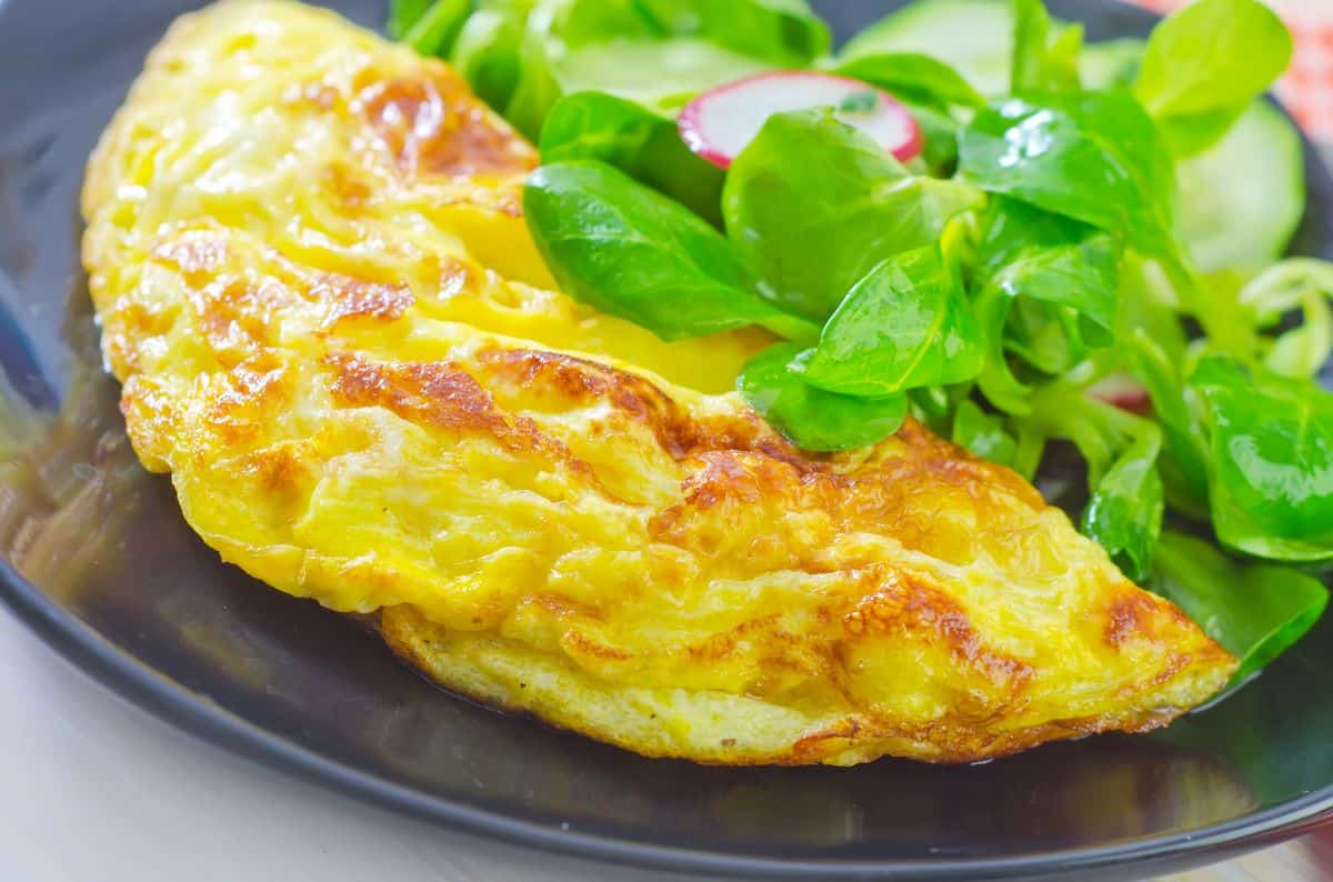 Omelette with salad on a black plate.