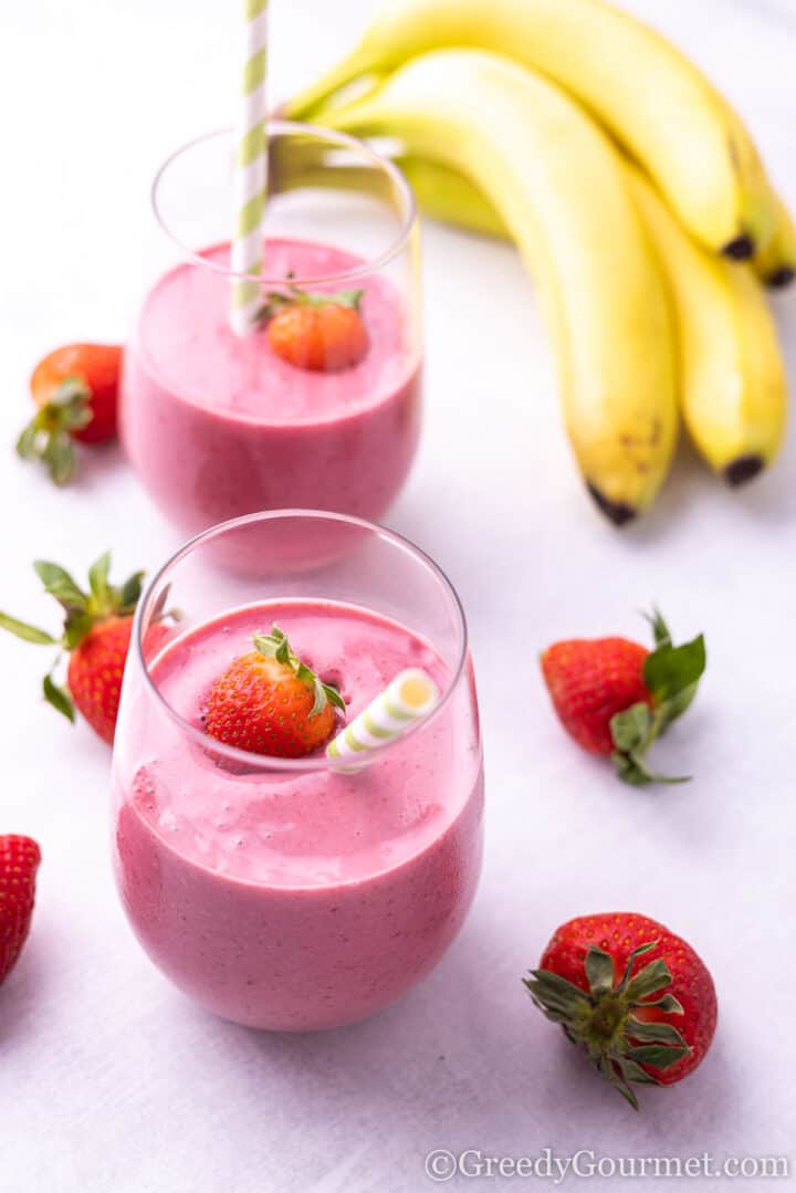 Strawberry Blackberry Banana Smoothie in a glass with a green paper straw and fruit around the glass.