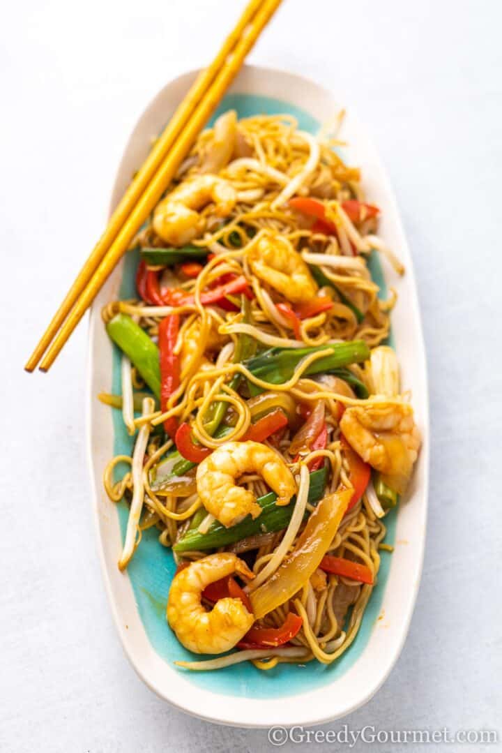 King prawn chow mein on a white plate with chopsticks. 