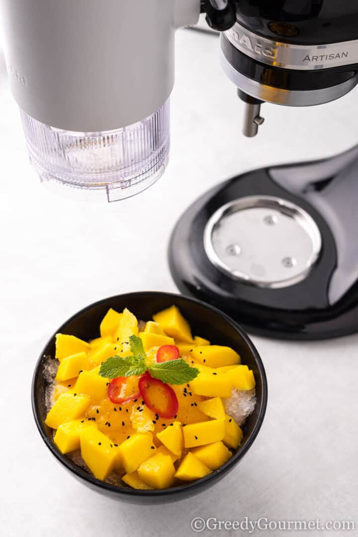 bowl of mango bingsu under ice shaving machine.