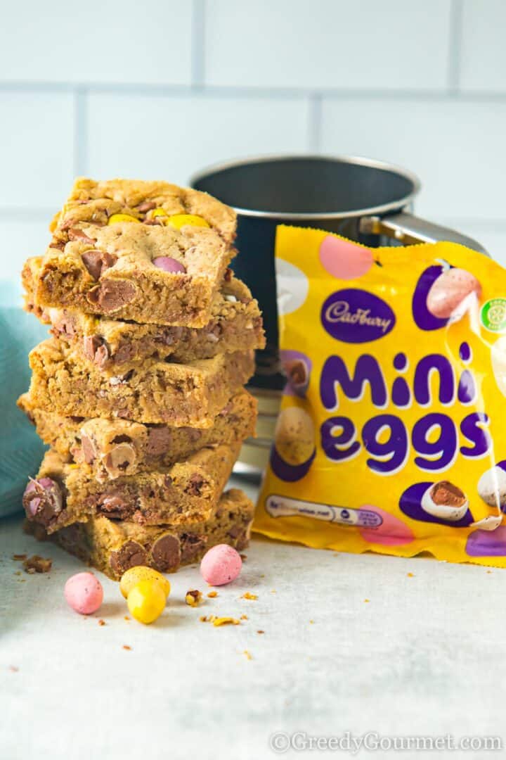 mini egg cookie bars stacked next to a bag of mini eggs.