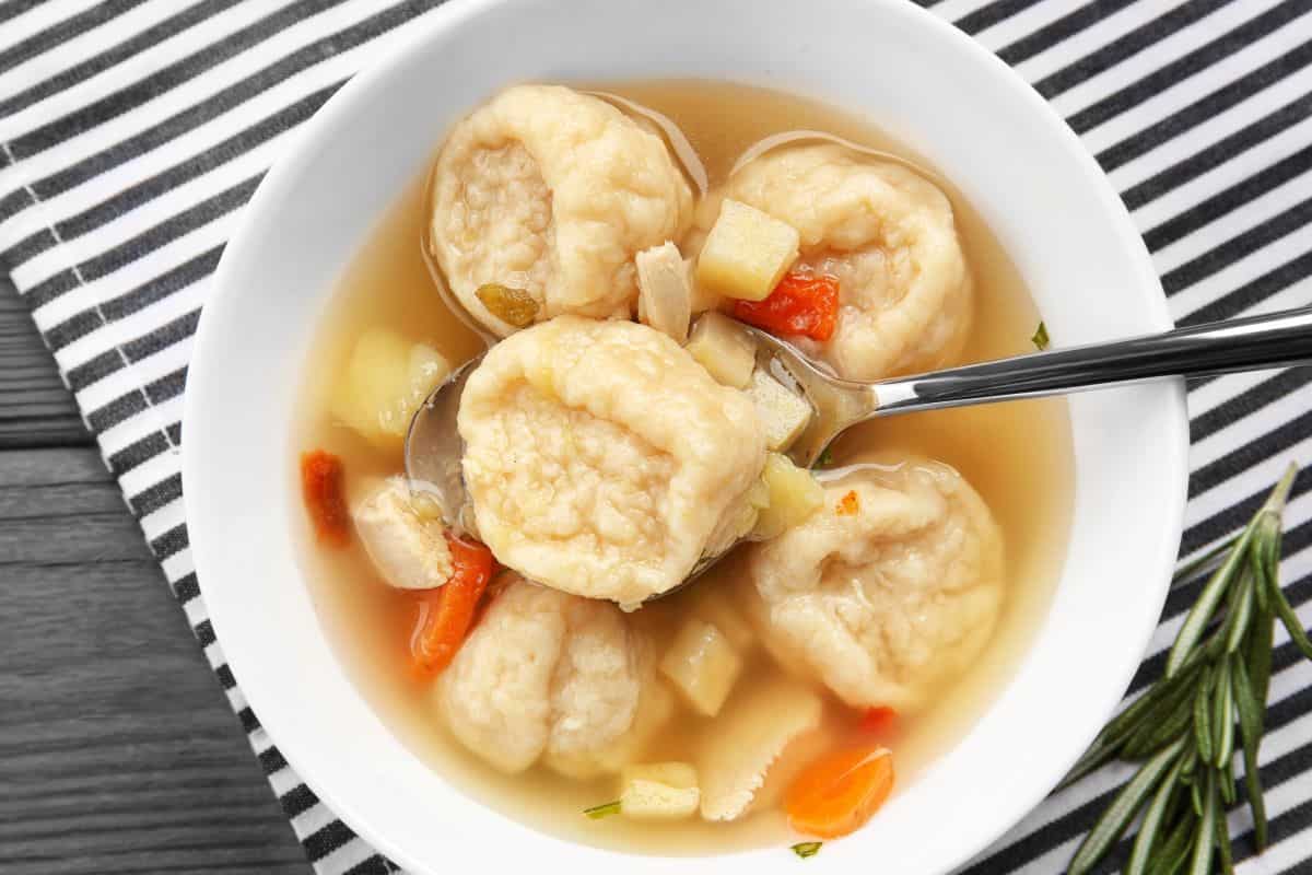 Portion of chicken and dumplings in a white bowl with vegetable pieces.