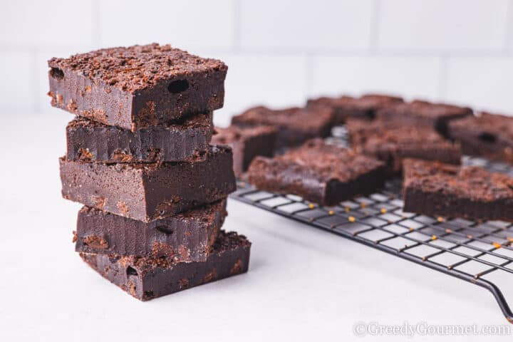 mochi brownie pieces stacked in a tower with a cooling rack behind.