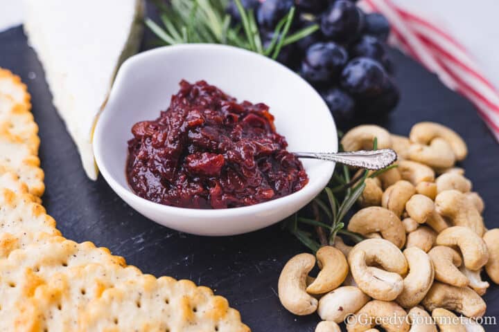 cranberry chutney on a board with cheese, crackers, rosemary and cashews.