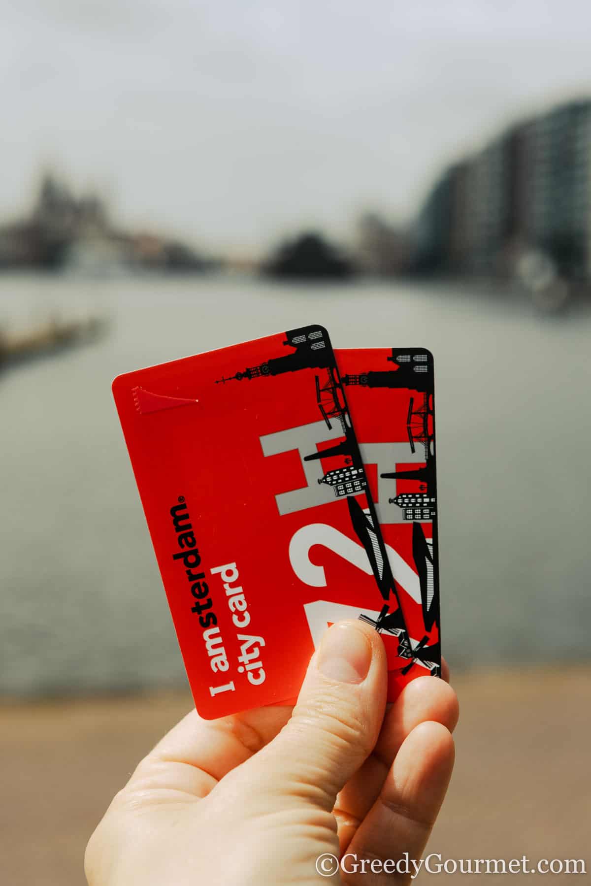 The hand of a person who is holding 2 red I Amsterdam city cards.