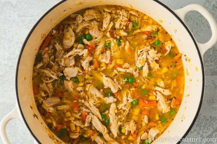 Broth with chicken and herbs in a pot.