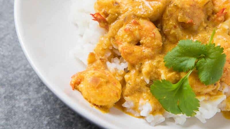 A finished bowl of Prawn Korma, prawns covered in yellow sauce on white rice