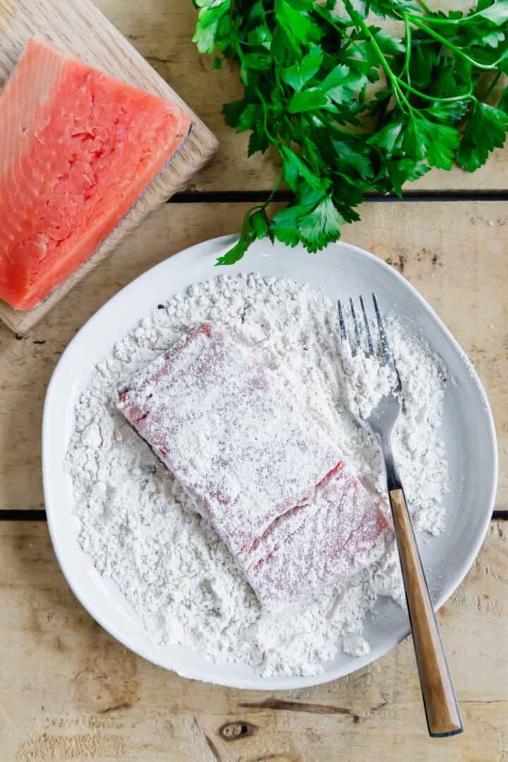 A plate of salmon piccata with parsley on a wooden table.