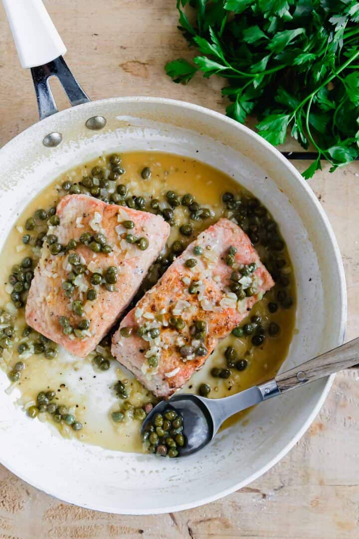 Salmon piccata with capers and parsley in a frying pan.