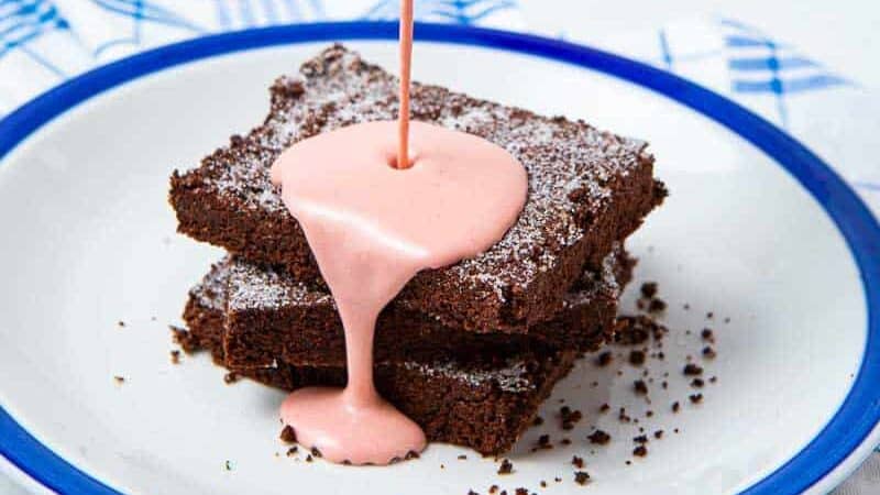 Pink custard being poured onto a chocolate cake