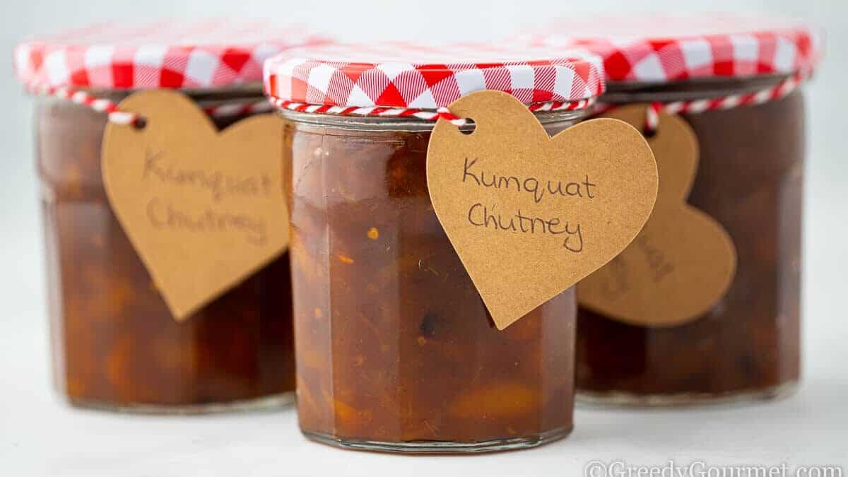 Three jars of kumquat chutney with red lids.