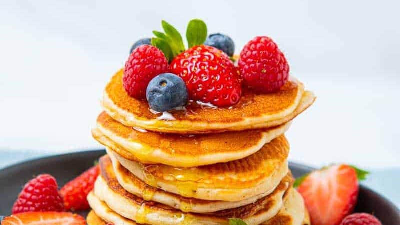 Tall stack of crempog with fresh berries and syrup