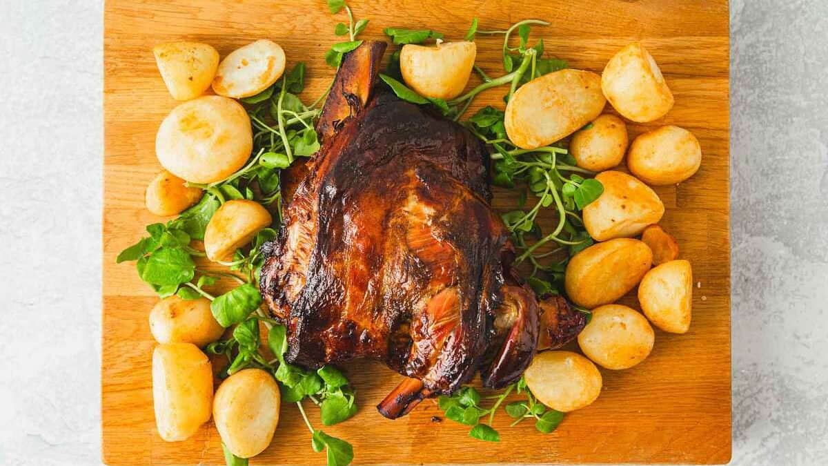 Slow roast lamb shoulder on a wooden board with potatoes.