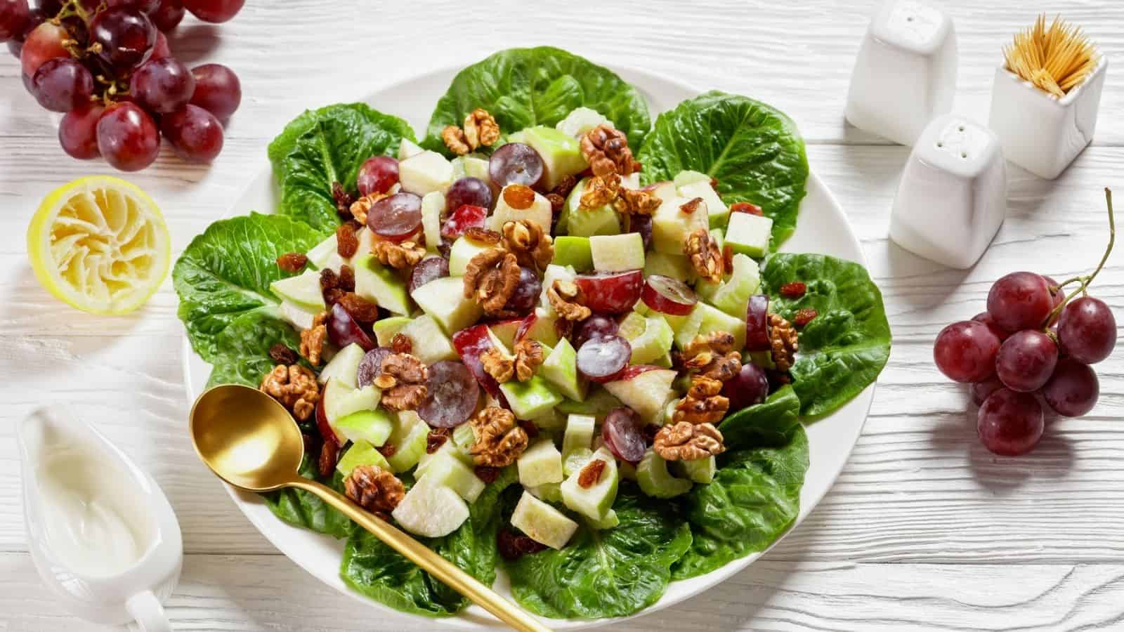 Waldorf Salad laying in lettuce, with apple cubes, walnuts and grapes, served in a white plate.