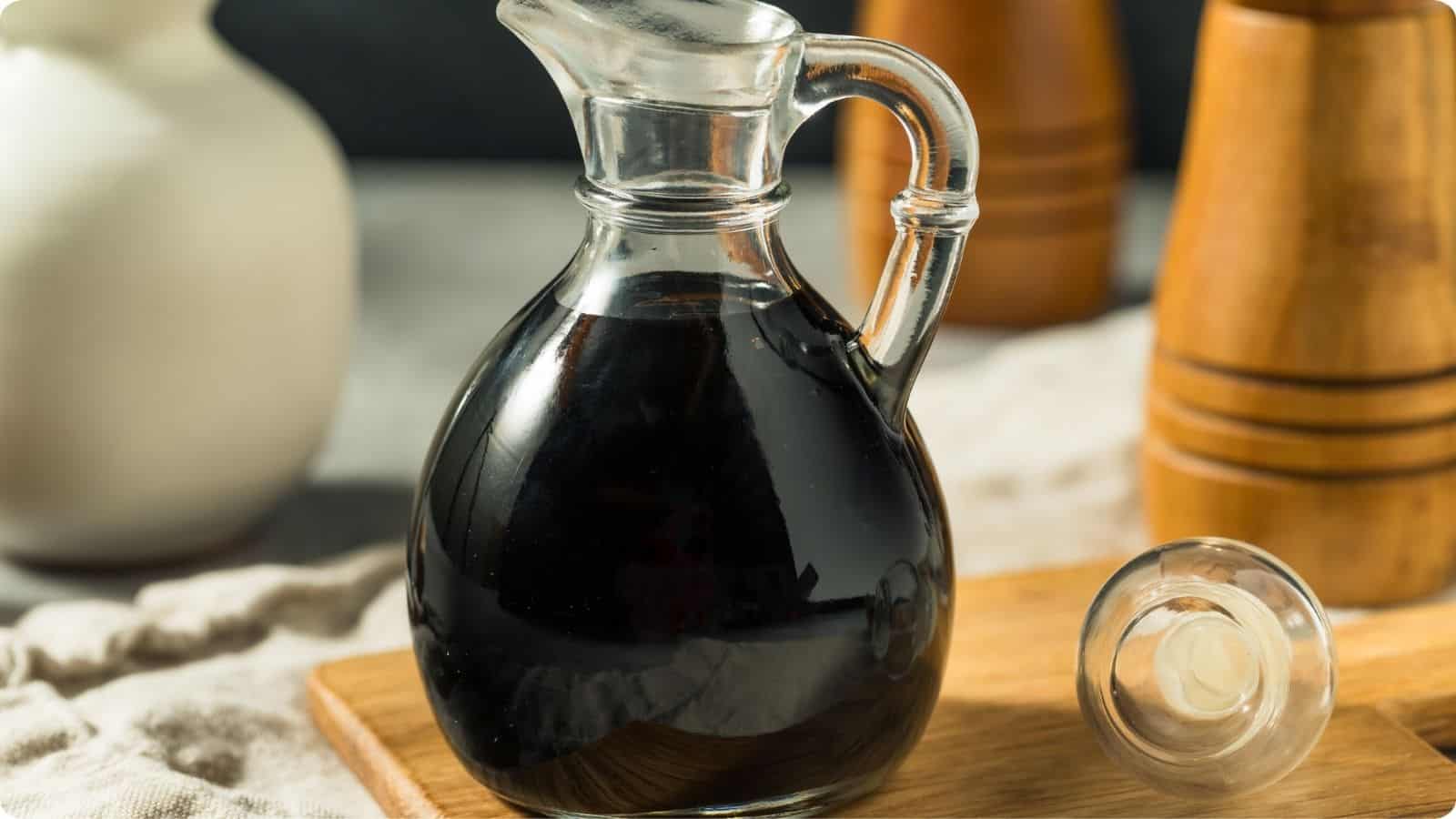 Balsamic vinegar in a glass container, resting on a cutting board atop a table.⁣