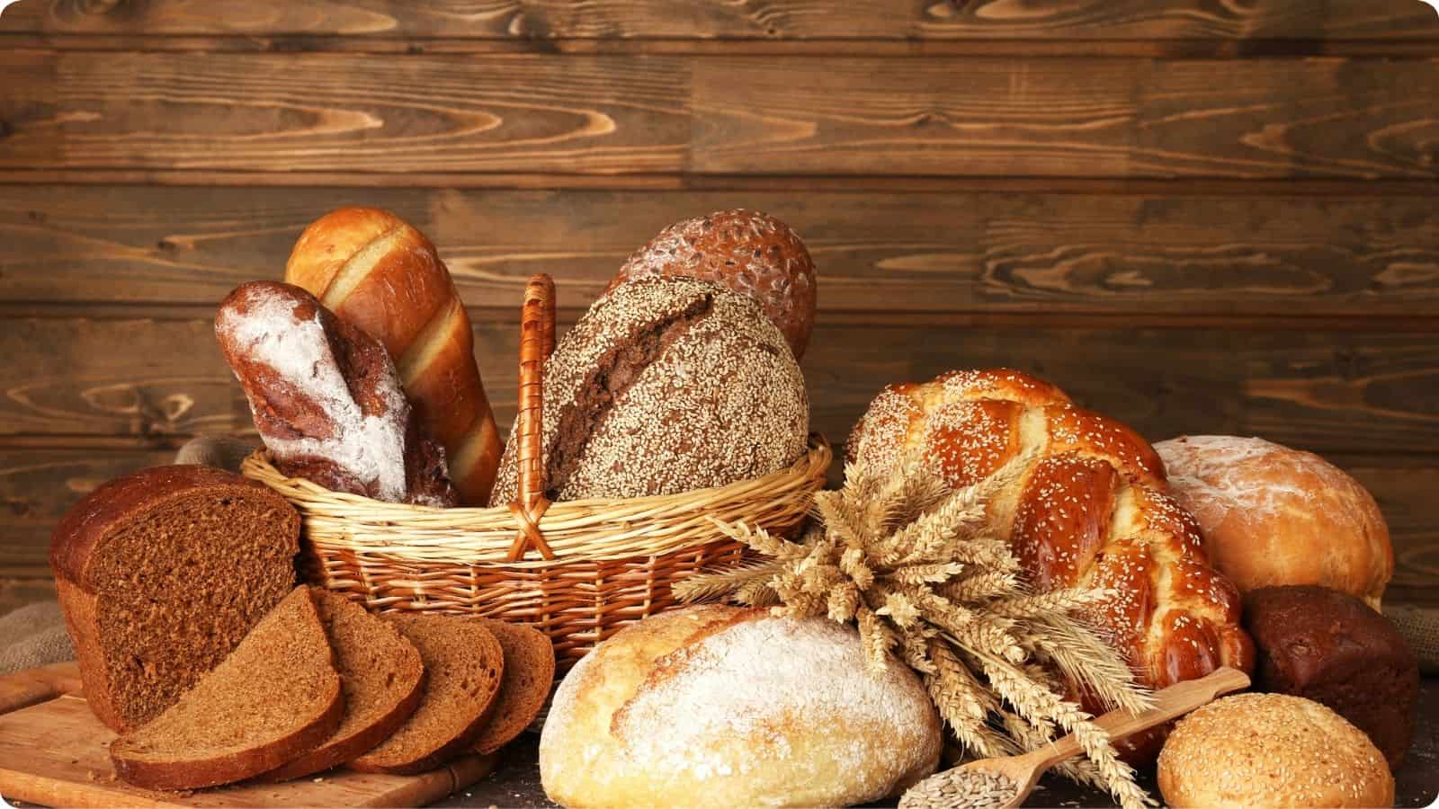 Assorted freshly baked bread in a basket, accompanied by various types displayed on a cutting board, all arranged on a table.