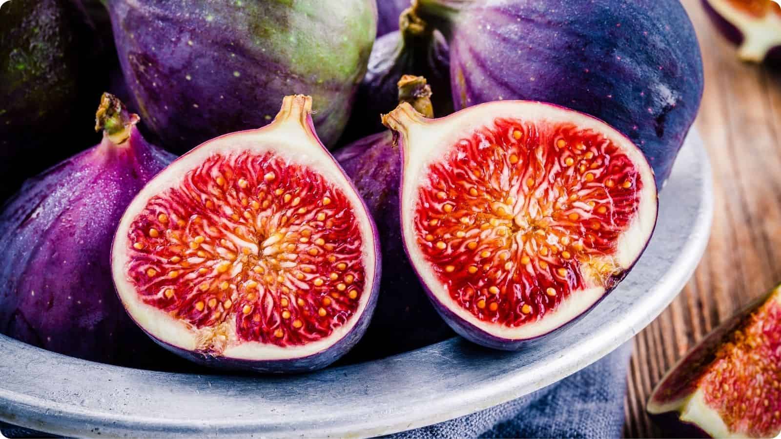 Figs in a mixing bowl place on top of a wooden table.
