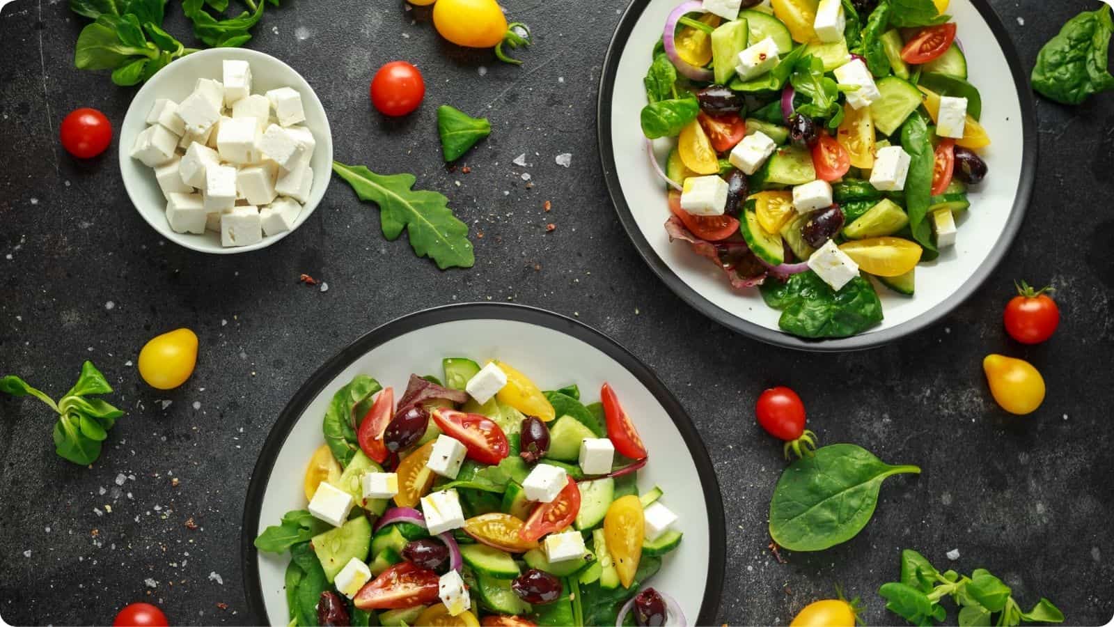 Two plates filled with fresh Greek salads, are displayed on a countertop.⁣
