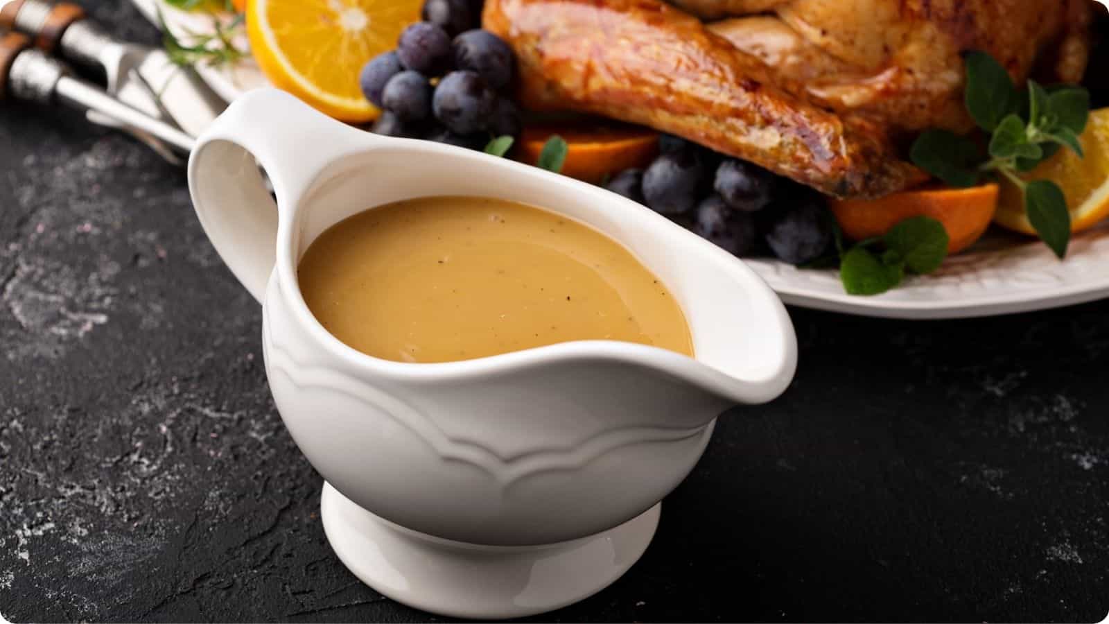 Gravy dispenser atop a charcoal-colored table, with a turkey in the background.