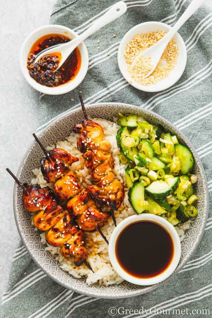 Yakitori chicken skewers served with rice and a cucumber salad.