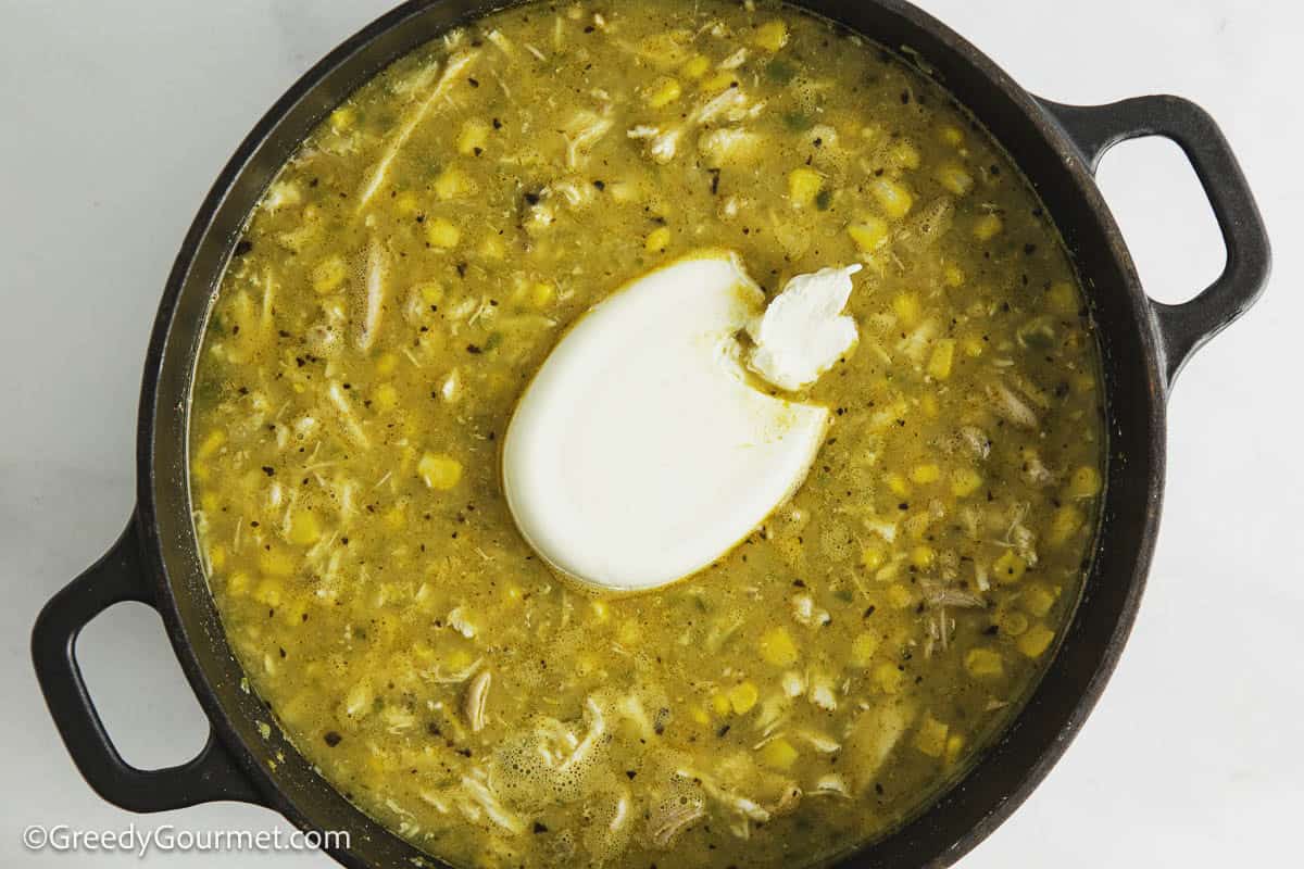 A pot of white chicken chili with a dollop of cream cheese on top.