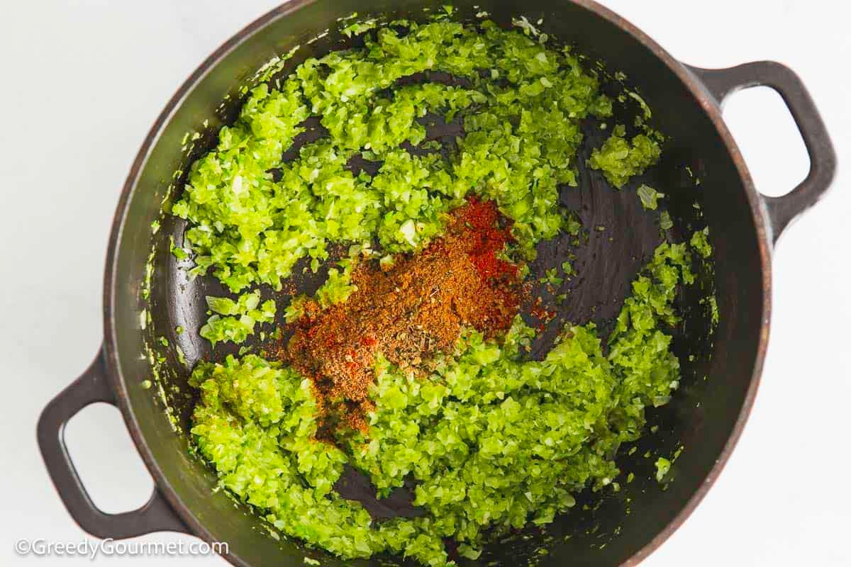 Diced onions, chilis and peppers in a cooking pot with seasonings on top.