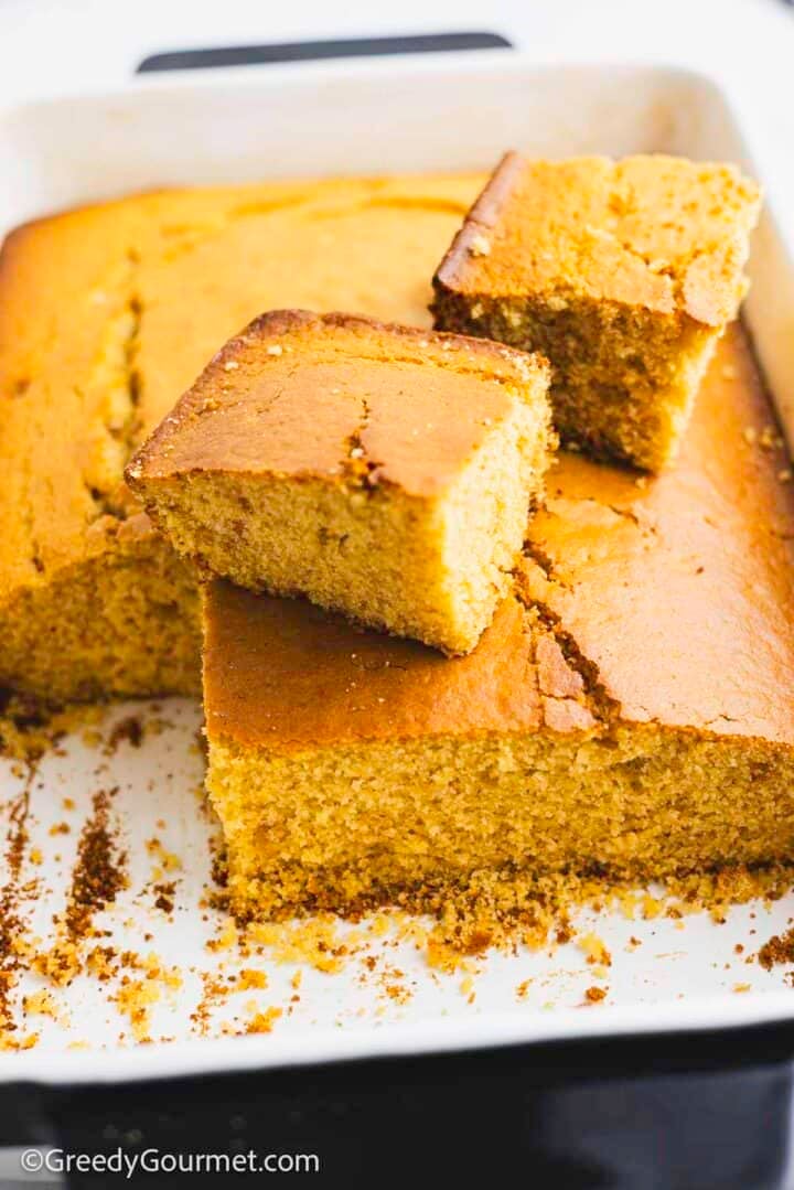 Cooked cornbread in a baking dish with a few squares taken out and piled on top.