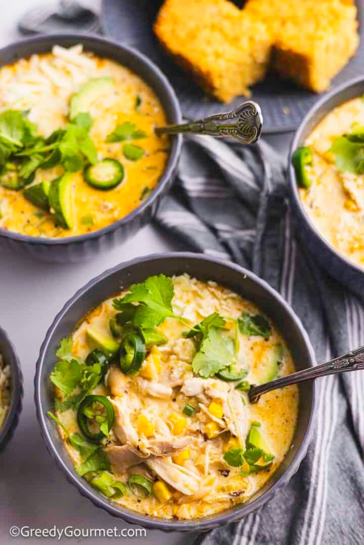 Grey bowls of white chicken chili with a spoon.